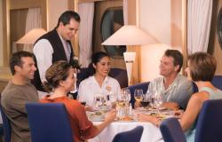 Celebrity Xpedition - Celebrity Cruises - lidé sedící u stolu v restauraci na lodi a číšník přinášející láhev vybraného vína